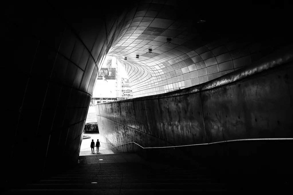 Dos figuras diminutas al final de un túnel de hormigón en blanco y negro