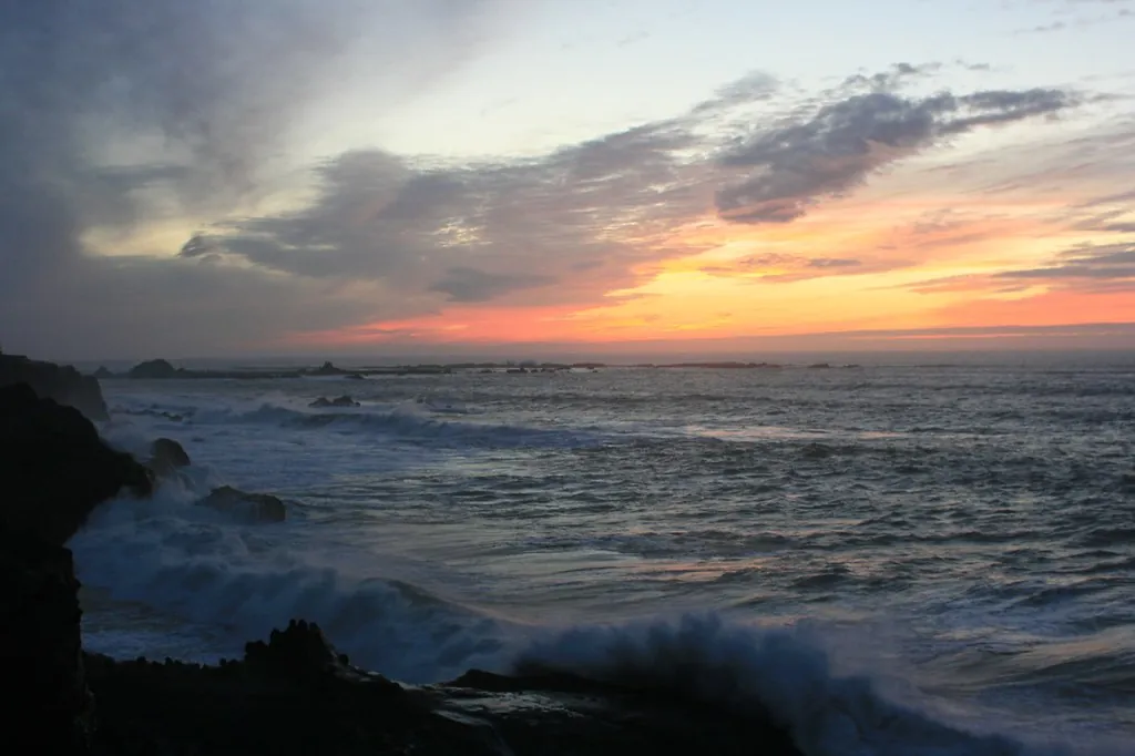 Olas rompiendo contra rocas bajo un cielo de tormenta al atardecer